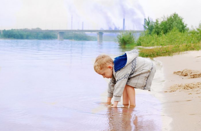 13858346 - playing little boy on the river coast near industrial plant