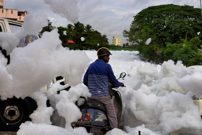 Bangalore, India was once known for its interconnected lake systems which provided a reliable source of water. As the city grew these lakes were encroached and the water became polluted day by day. The largest Bellandur Lake in Bangalore now carries huge volume of snowy froth which blocks the adjacent canals. This froth which would otherwise been a sight to behold stinks and on contact with skin causes irritation. Following a heavy rain the froth from the canal rises up and lands on the roads causing inconvenience to those travelling on two wheelers. This is a major concern with many such lakes in Bangalore which are getting polluted with harmful chemicals like nitrates, potassium, sulphates, etc. Although the residents have raised their concern by informing the local media for cleaning the lake, till date the Government has not taken adequate measures. The lake now emits intoxicating smell and blew froth all around whenever there is wind. Despite all such issues new residential complexes are still coming up. The affected area would be around 200 meters and if it too windy the froth flies even further entering the neighbouring houses. The people residing nearby the lake are suffering from several health issues.